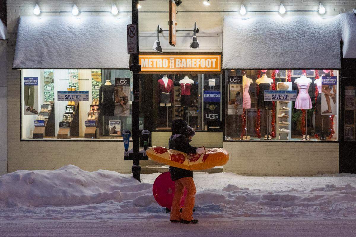 Pedestrians walk down College Avenue with blowu-p sleds during a snowstorm on Sunday.