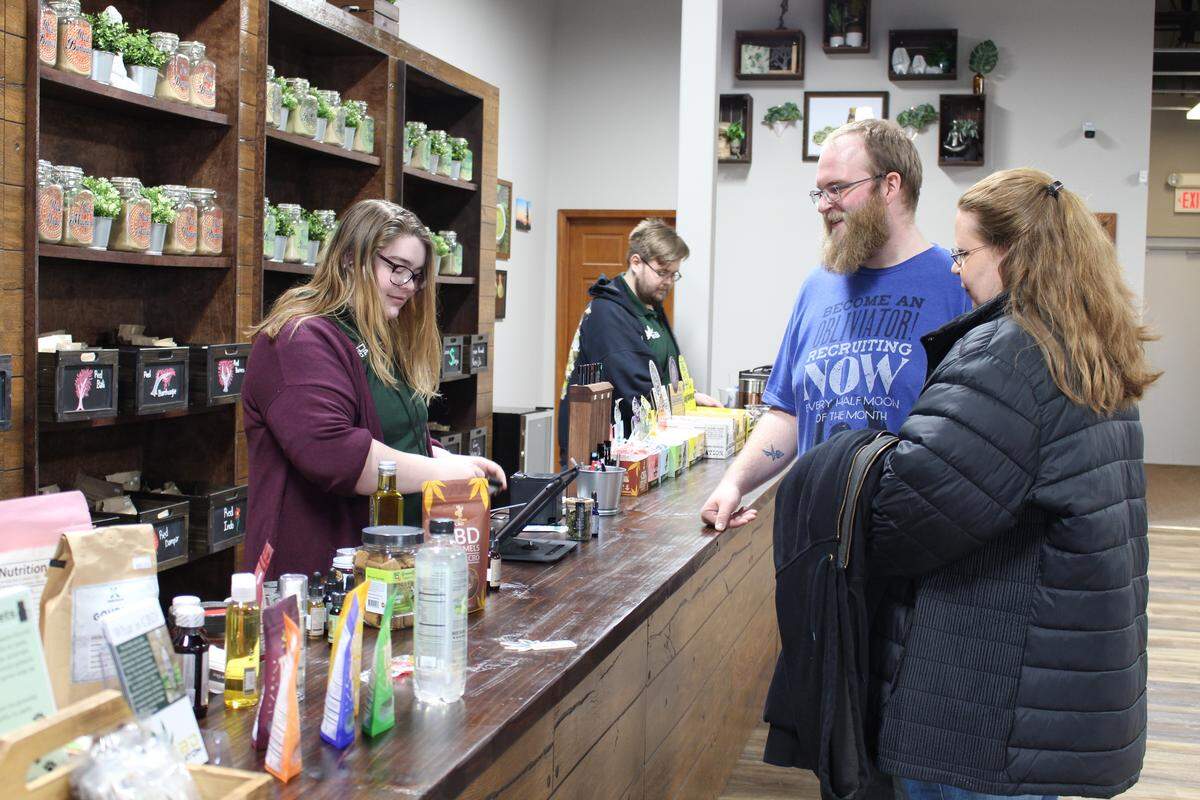 Clerk Anna Scott, left, rings up a jar of hemp flowers for Blake Clarke, shown with his mother, Shawna Clarke, at the new CBD Kratom store in Belleville.