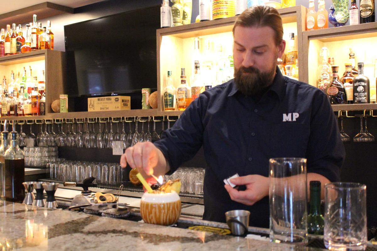 Zach Robinette, bar manager and mixologist at Moussalli’s Prime in Edwardsville, sets fire to a lime in one of his specialty drinks, the Amateur Physician.