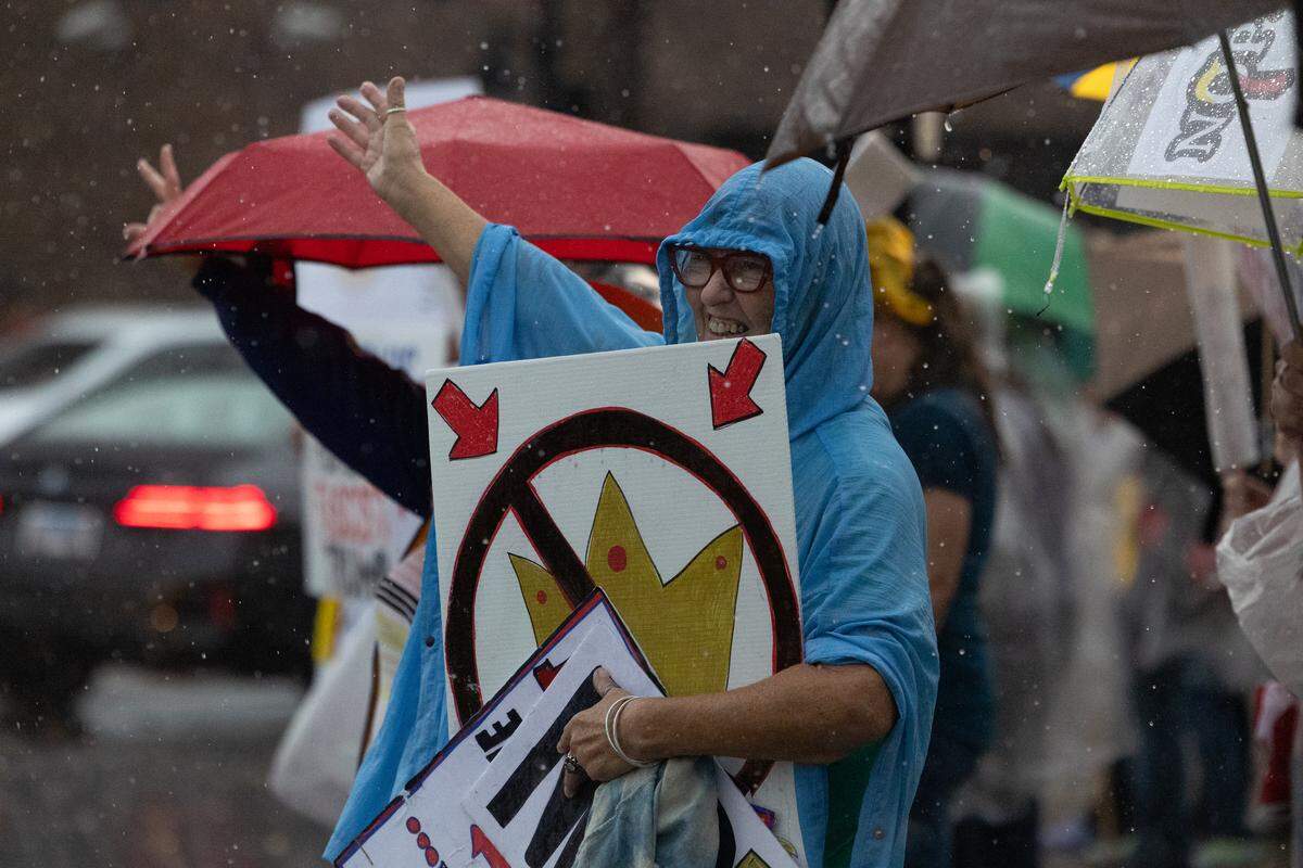 Protesters wave to passers-by during a deluge at the No Kings protest on the Belleville Public Square on Saturday.