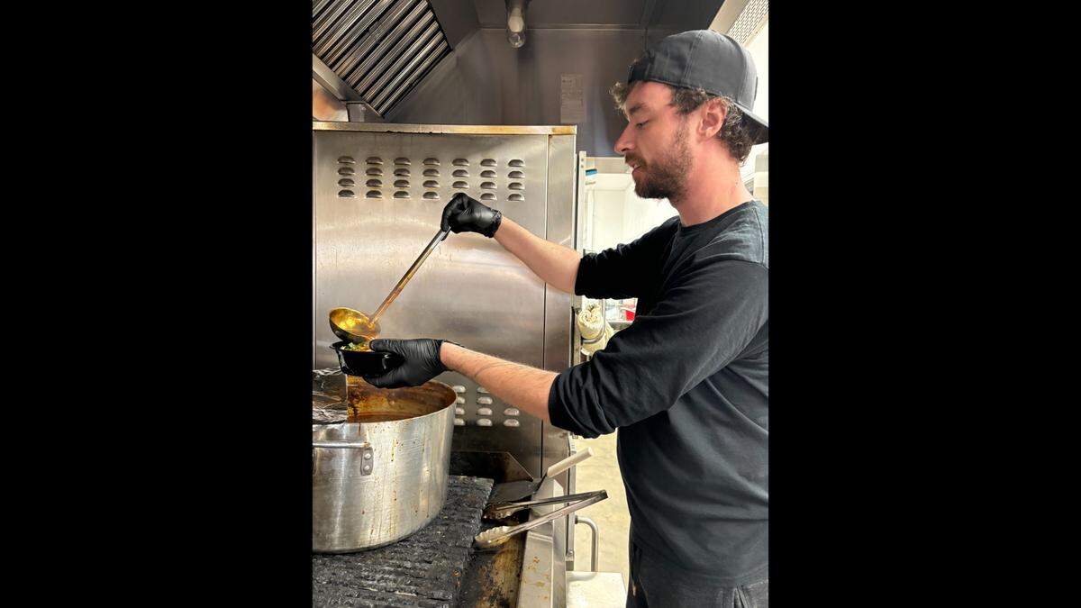 Shaun Hudson ladles ramen into a serving bowl.