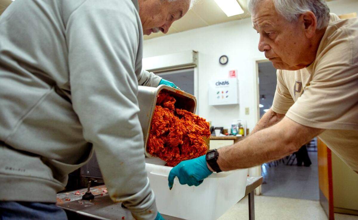 Charlie Suarez, 74, right, and Mike Albertina, 73, of Belleville, scoop seasoned ground pork on Dec. 21 at the village community center in Fairmont City.