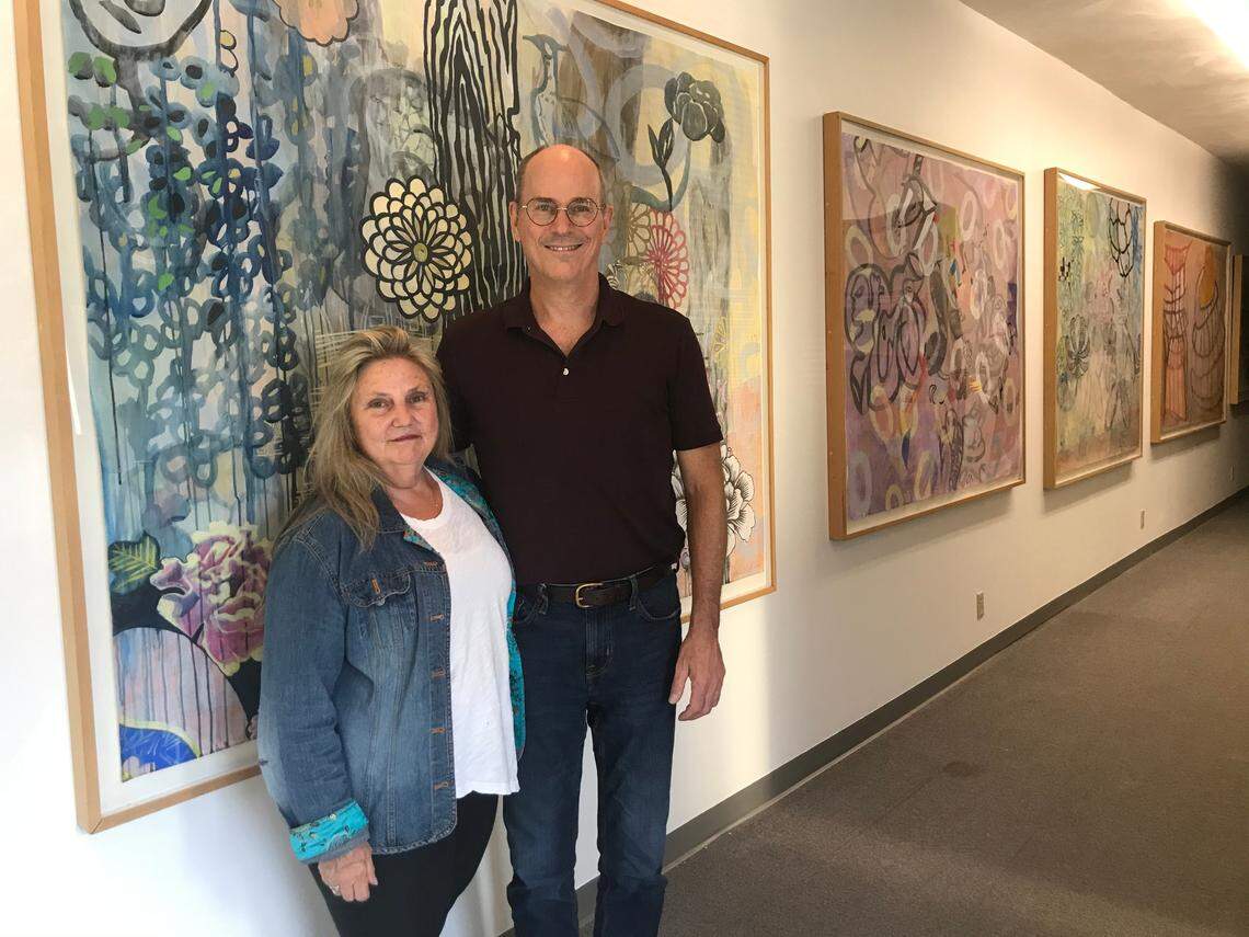 Artist Catharine Magel and businessman David Kniepkamp pose in front of her artwork displayed at his office in Fairview Heights. They’re partnering in the Art Village development.