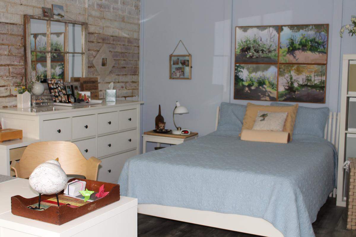 The upper-level bedroom of the Farthing home in Belleville has a whitewashed brick wall, an eclectic mix of furniture and a wall of windows that overlook woods.
