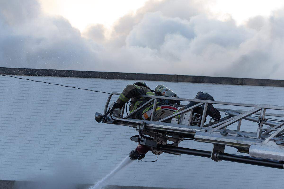 A firefighter sprays a fire while a large cloud of smoke billows beyond.