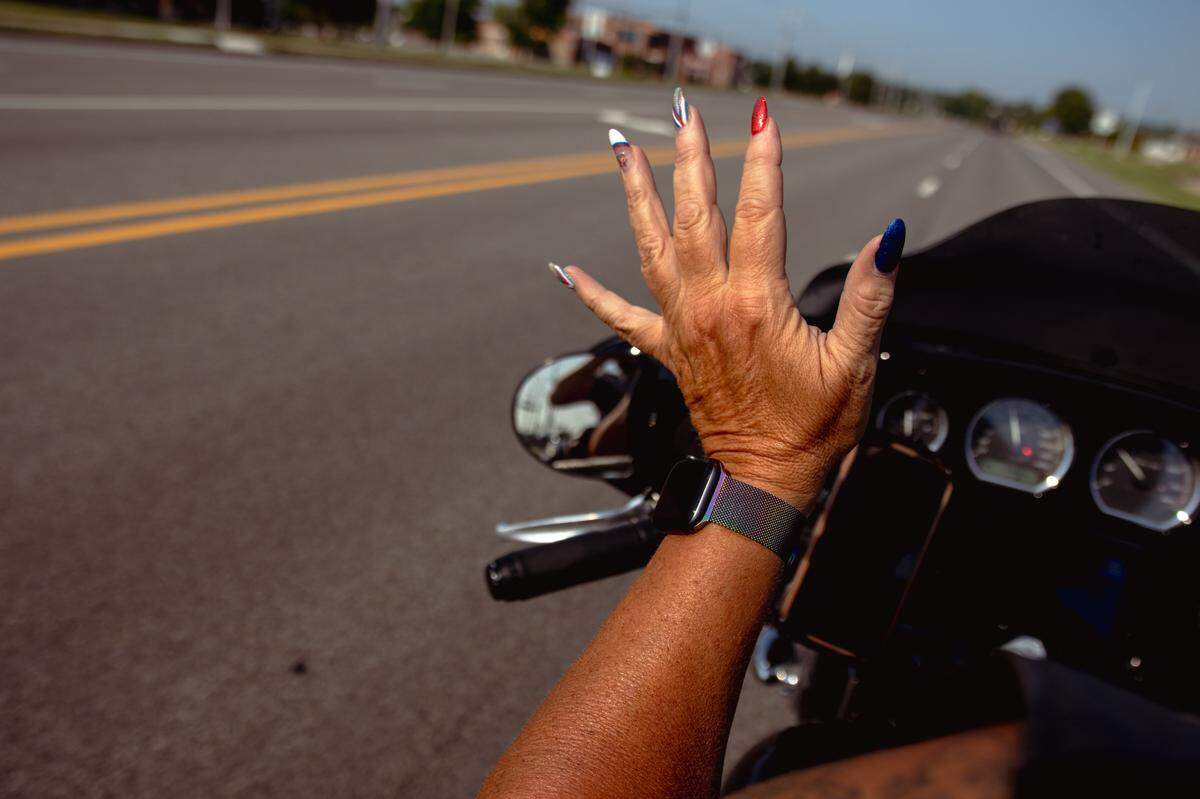 Tina Weber, 54, feels the rush of wind flow through her hands while listening to music during a morning motorcycle ride on Sunday, July 14, 2024, in Collinsville, Illinois.
