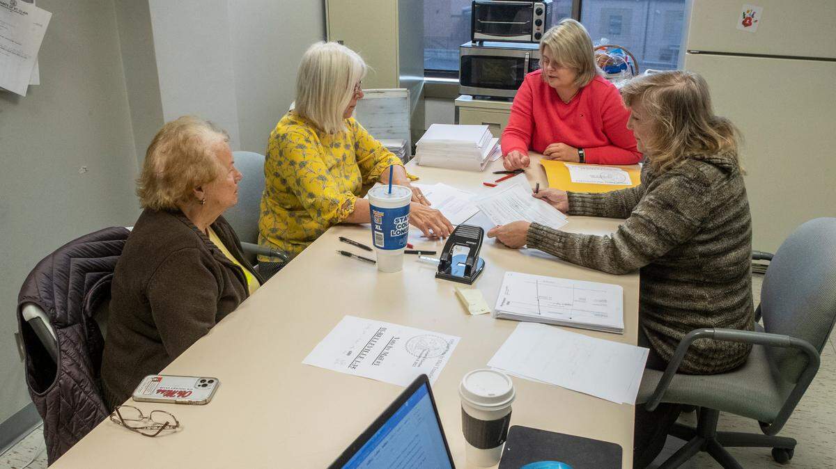 Democratic and Republican election judges review voter signatures on mail-in ballots with a poll watcher at left.