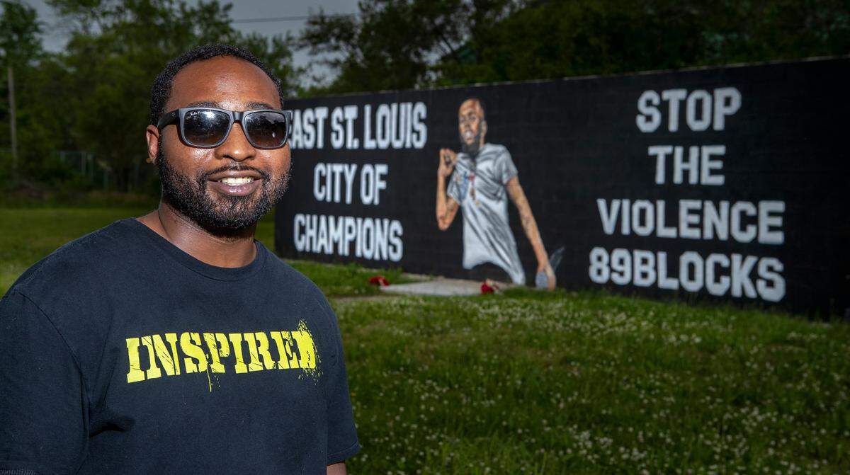 East St. Louis artist, Mykael Ash, stands near a recently finished mural honoring slain East St. Louis rapper “Cold Kase,” Cedric Gooden.