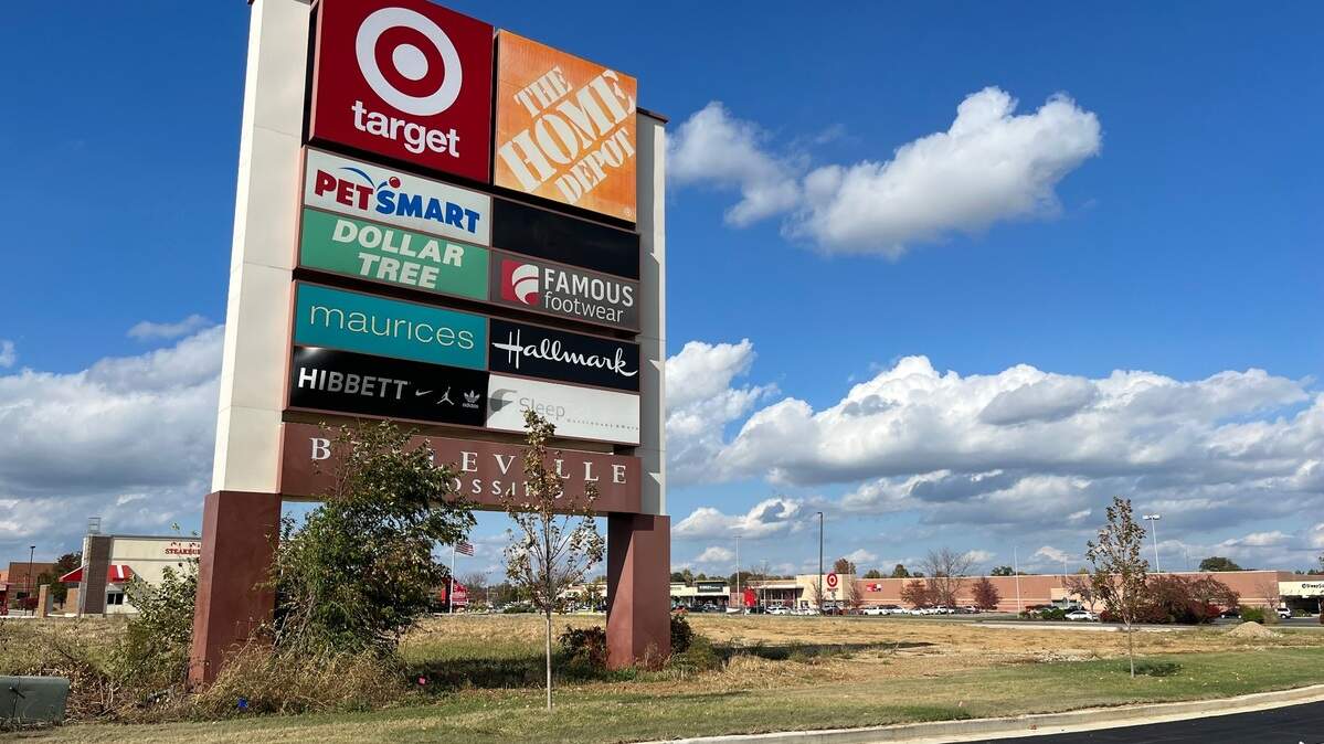 Overgrown weeds and a scraggly tree surround a giant pylon sign for Belleville Crossing shopping center, off Illinois 15. It stands next to property with new landscaping where a Take 5 car wash is being built.