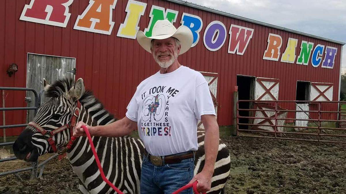 Alan Blumhorst, owner of Rainbow Ranch and petting zoo in rural Nashville, is shown with Ziggy the Zebra next to his colorful red barn.
