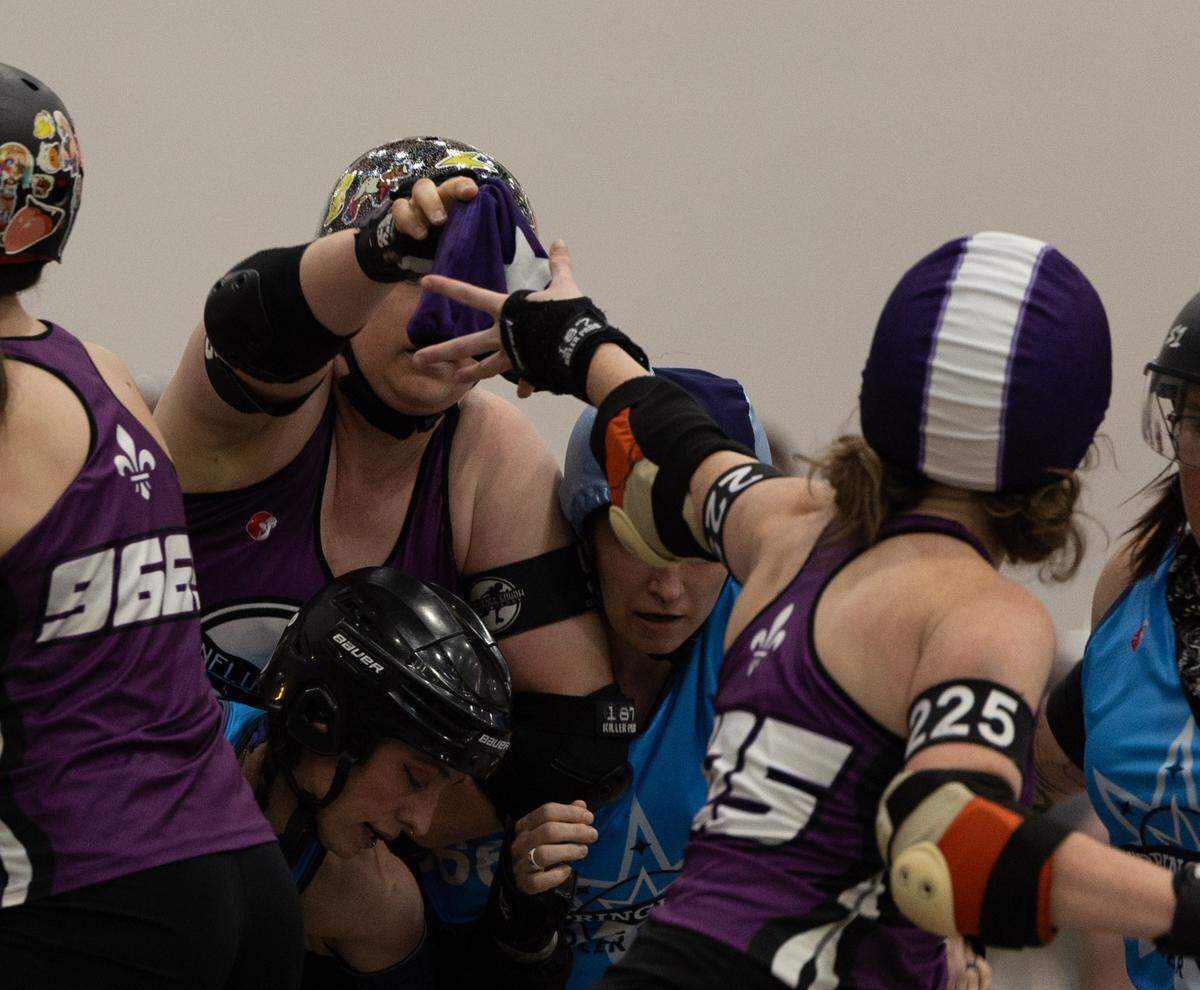 A Confluence Crush jammer passes the scoring helmet sleeve to another jammer to continue scoring points.