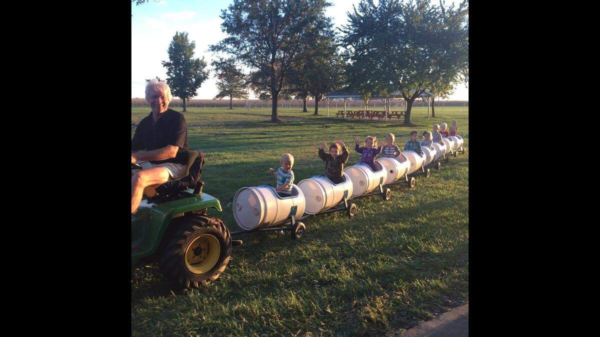 Charles “Chuck” Poettker uses a four-wheeler to pull children on a kiddie train of barrel-shaped cars through a field.