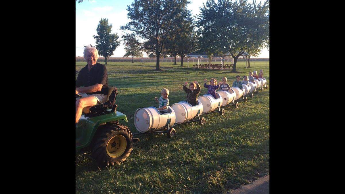 Charles “Chuck” Poettker uses a four-wheeler to pull children on a kiddie train of barrel-shaped cars through a field.