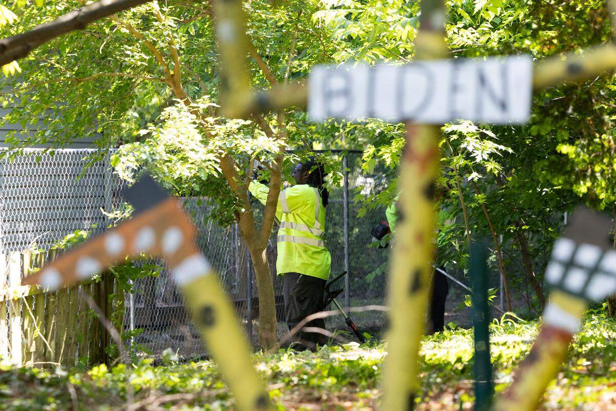 A Belleville city worker trims around a fence outside the home of Stewart Lannert on South 29th Street. In the foreground is a metal stick figure representing former President Joe Biden, one of the many political statements in his yard.