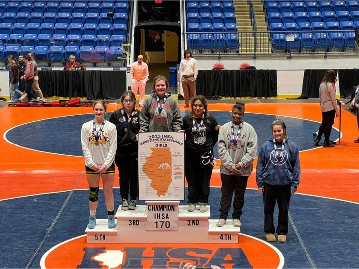 Highland sophomore wrestler August Rottmann (top center) stands with the top six competitors in the girls’ 170-pound class after winning her first IHSA state title and the first state championship in Lady Bulldogs program history Saturday, Feb. 25, at Grossinger Motors Arena in Bloomington.
