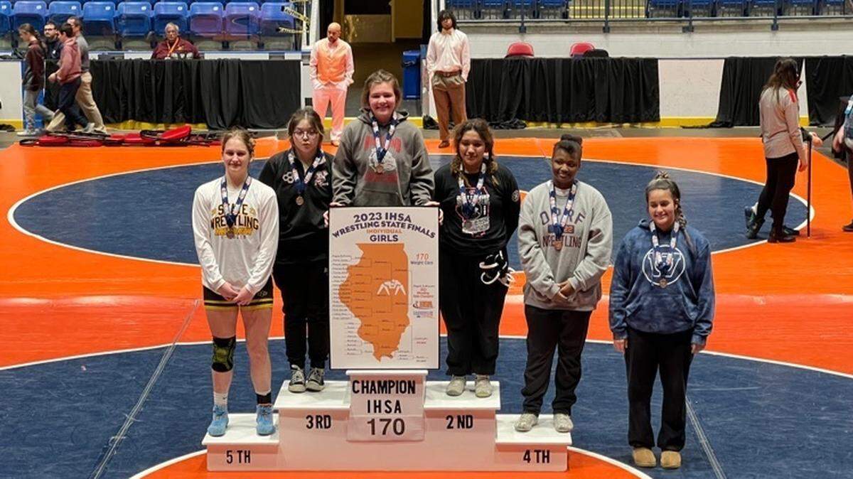 Highland sophomore wrestler August Rottmann (top center) stands with the top six competitors in the girls’ 170-pound class after winning her first IHSA state title and the first state championship in Lady Bulldogs program history Saturday, Feb. 25, at Grossinger Motors Arena in Bloomington.