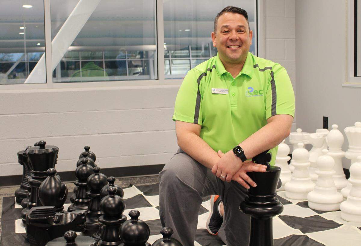 Chris Tierney-Hurst, who became The Rec’s facility manager last summer, poses with a giant chess board in the lobby during a party for charter members Friday night.