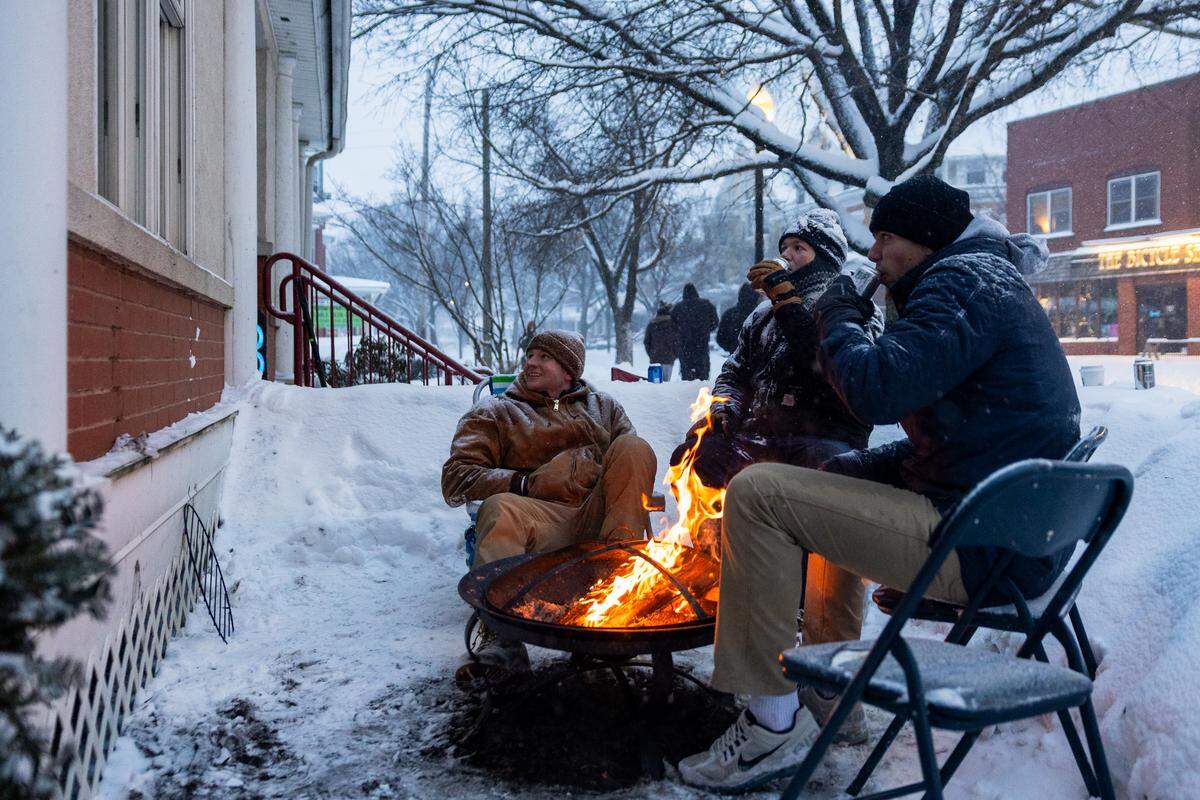 From left to right, Penn State students Jake Heckman, Chad Henning and Andrew Gouldon sit by a fire on their front lawn while watching TV during a snowstorm on Sunday.