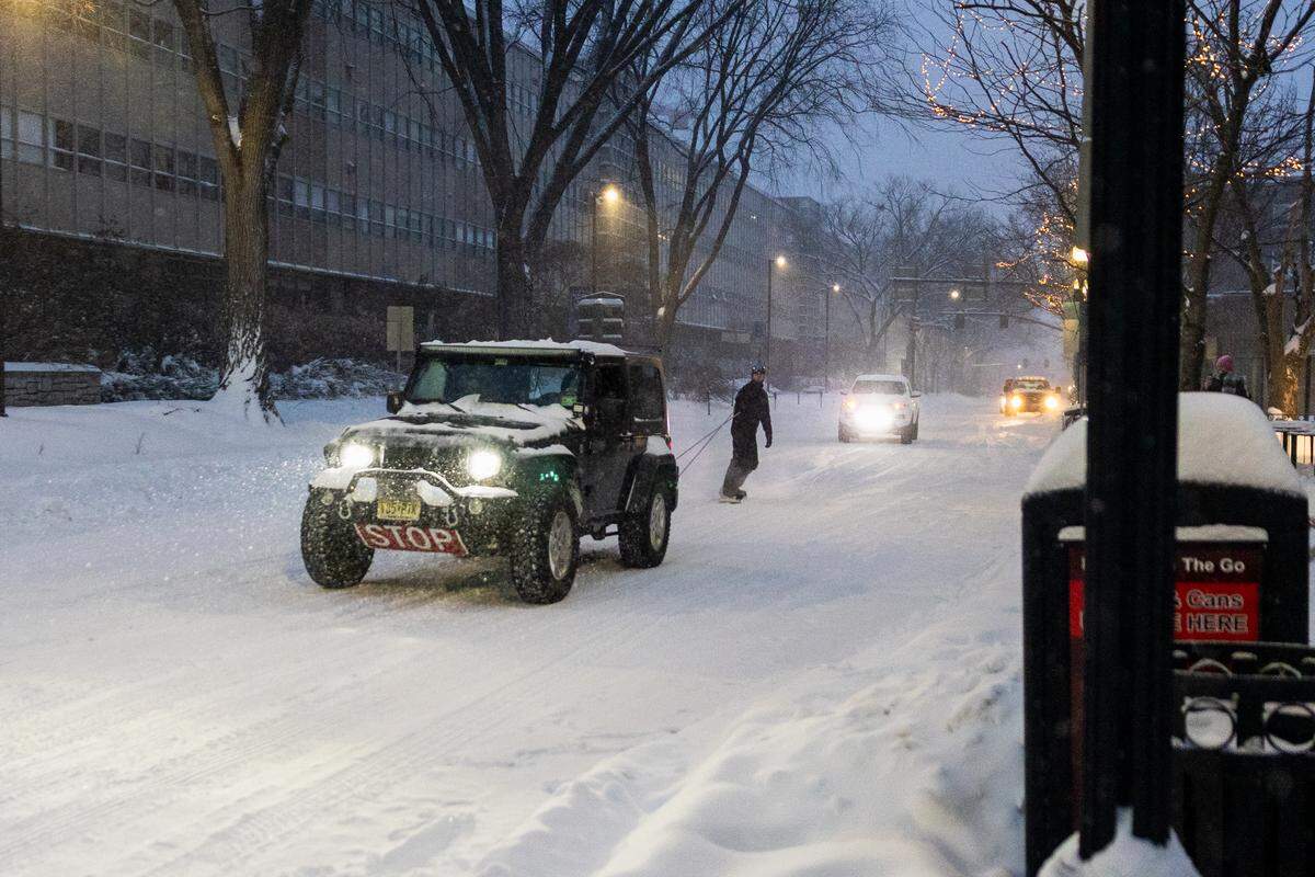 A pedestrian snowboards behind truck on College Avenue during a snowstorm on Sunday.