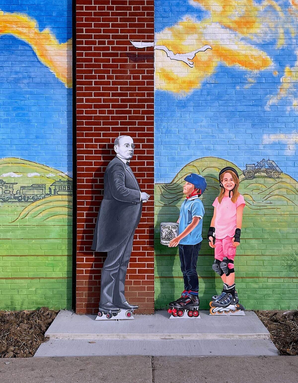 Made possible in part by a $10,000 matching grant from the National Endowment for the Arts, a mural was designed and painted on the side of the Weinheimer Community Center at the corner of Main and Pine Streets in Highland, by Robert and Liza Fishbone of On the Wall Productions from St. Louis. They were assisted onsite by Andy Cross (set painter for The St. Louis Muny Opera), and Lisa Roth. Deborah “Moe” Moellering painted the three cut out figures installed next to the mural.