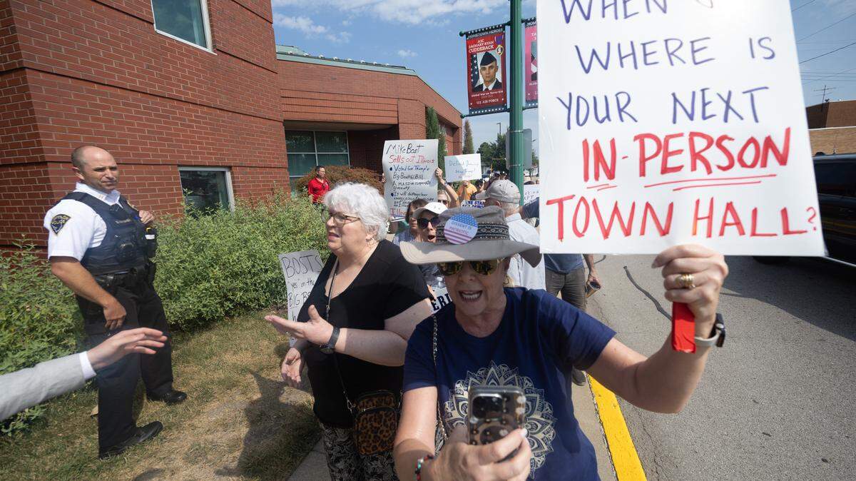 Protesters outside of O’Fallon City Hall follow U.S. Mike Bost to a waiting police car, demanding to know when his next in-person town hall will be.