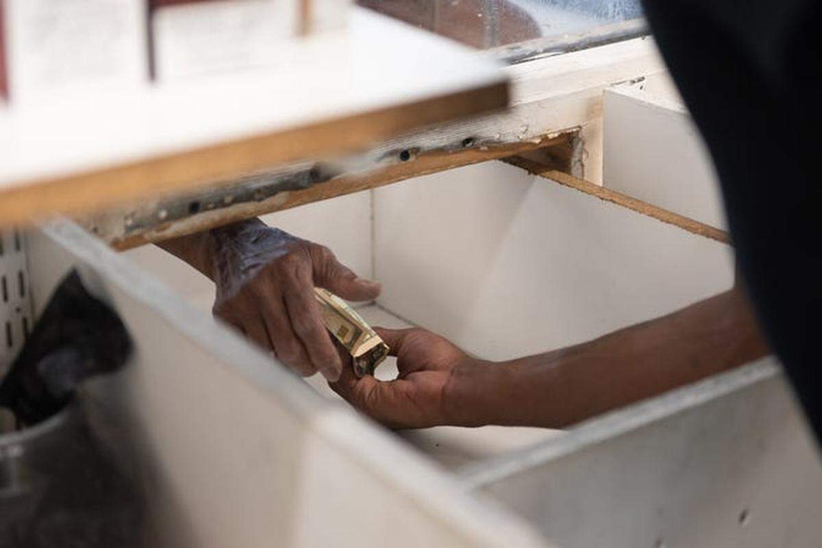 A customer pays for merchandise through a partition at Charlie’s Convenient Market. The store is one of the only nearby food sources for many residents.