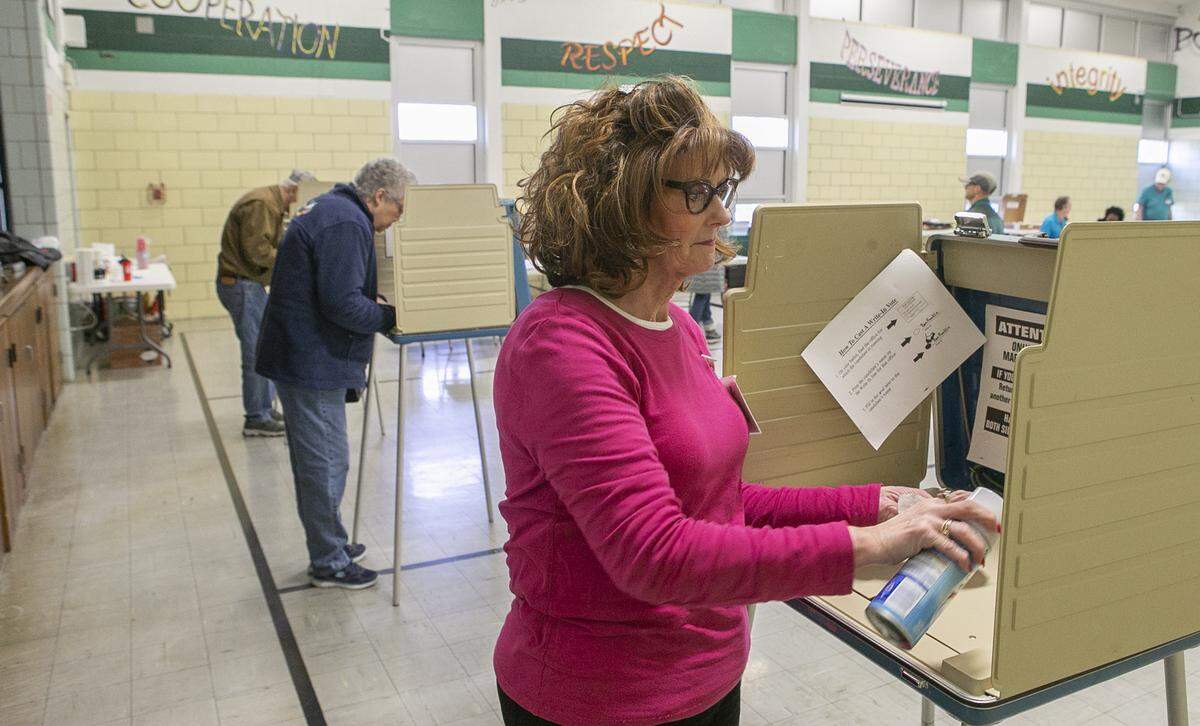 Election judge Judi Brunstein uses a disinfectant spray to clean a voting booth at the polling place inside Douglas Elementary School in Belleville during Tuesday’s primary election. Staff were using a variety of methods to disinfect and prevent the potential spread of coronavirus.