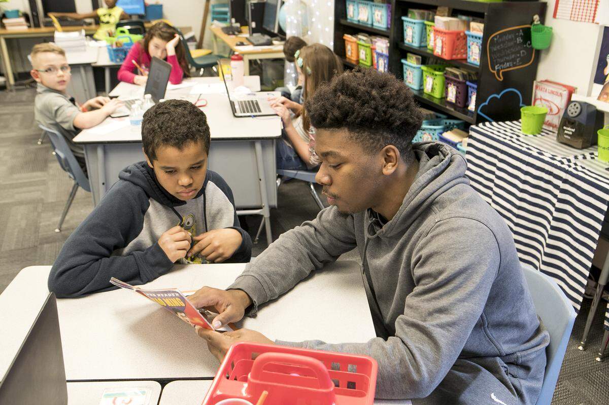 Fourth-grade student Jordyn White and Sparta High School senior Jonathan Williams read a book about NBA player Yao Ming. High school students work with elementary students to gain work experience and see if they might enjoy a teaching career.