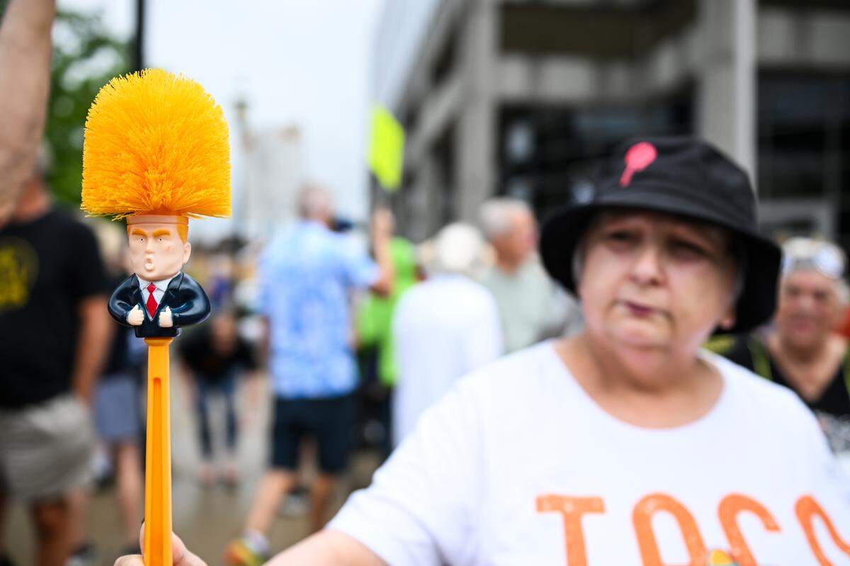 A “No Kings” protester in Belleville holds up a toilet brush depicting President Donald Trump.