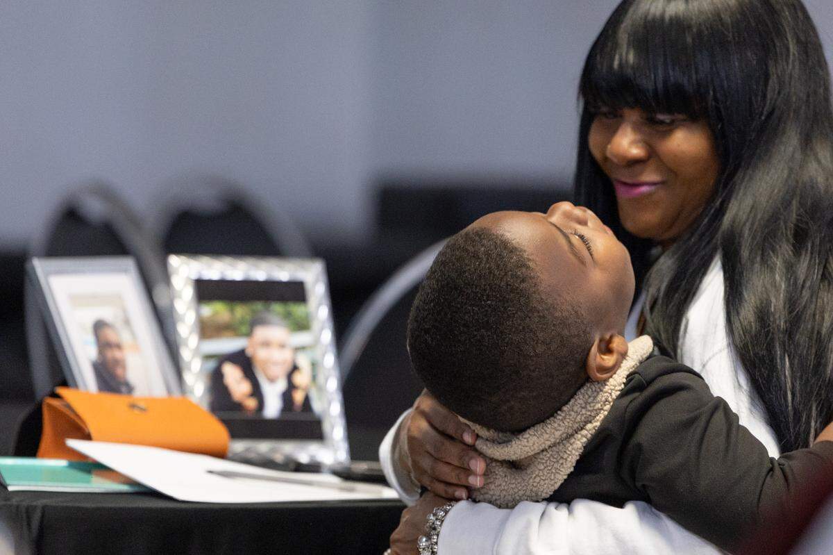 Sheleasa Blackwell of St. Louis holds a child in her lap while photos of her son Corey, who was murdered in 2022, sit on the table.