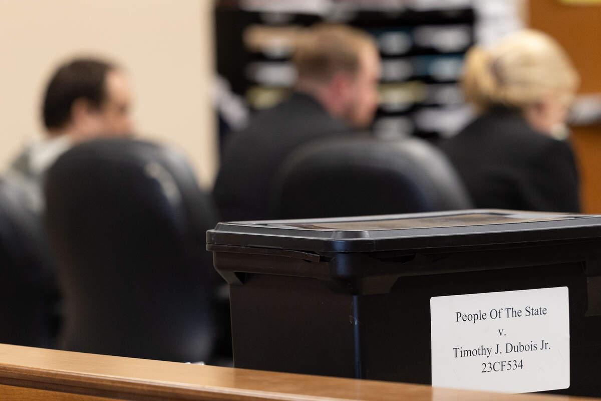 A box labeled “People Of The State v. Timothy J. Dubois Jr.” sits near the gallery during the sentencing hearing for Timothy J. Dubois while the defense presents arguments in the background.