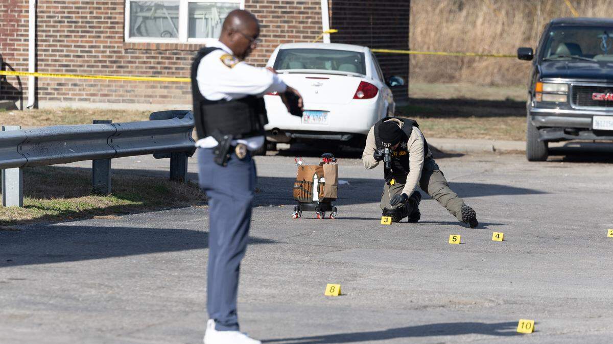 Cahokia Heights Police Chief Thomas L. Trice (foreground) checks the time while an evidence collector places telemetry and evidence markers on the ground at the scene of a shooting at the Greystone Apartments in Cahokia Heights. By noon Wednesday, more than 10 evidence markers were placed at the scene.