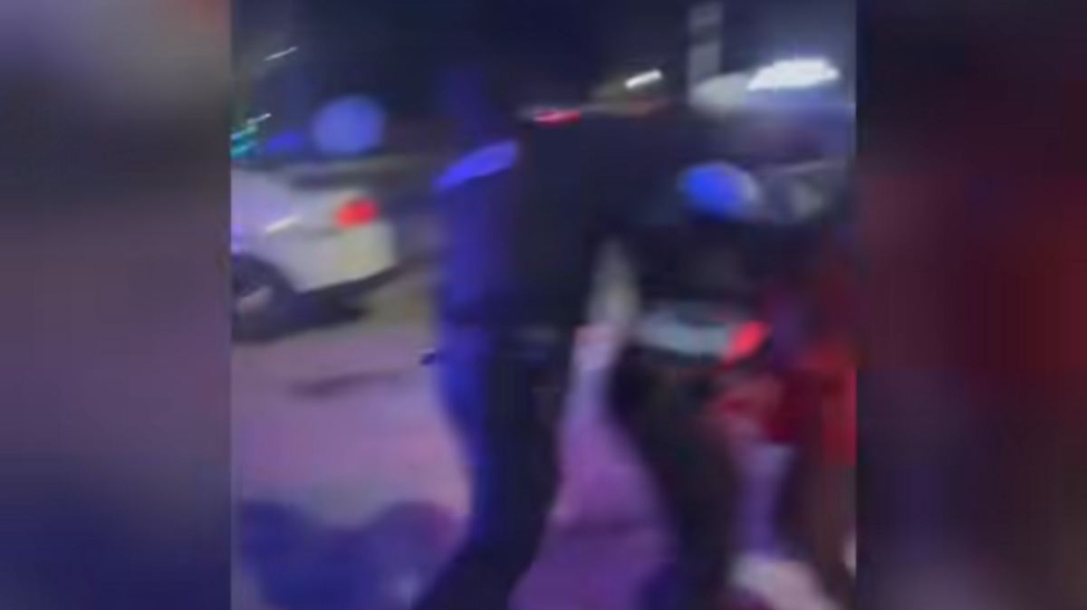A frame from cellphone video shows a Brooklyn police officer apparently throwing a punch at a woman in a red dress. Another officer stands between them. Illinois State Police are investigating the incident.