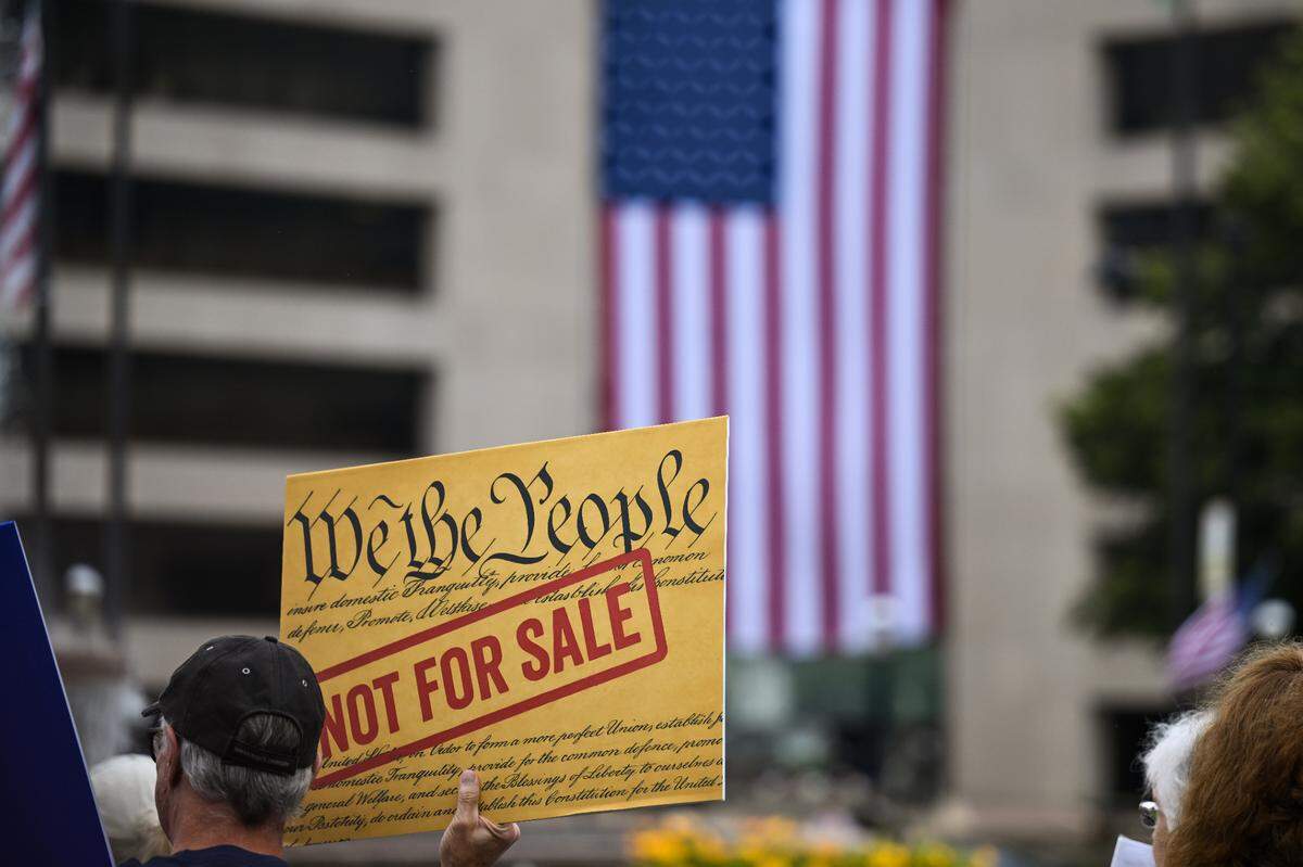 A “No Kings” protester in Belleville holds a sign reading “We the people not for sale.”