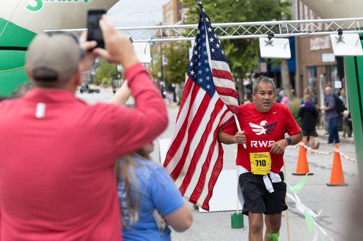 Joe Gomez, U.S. Navy veteran of Compton, Illinois, crosses the finish line at the Belleville Marathon on Sept. 28, 2024. Gomez carried the American flag as a representative for Team Red, White and Blue, a veterans group that emphasizes the benefits of physical exercise. “I did this for everyone who didn’t come home.”