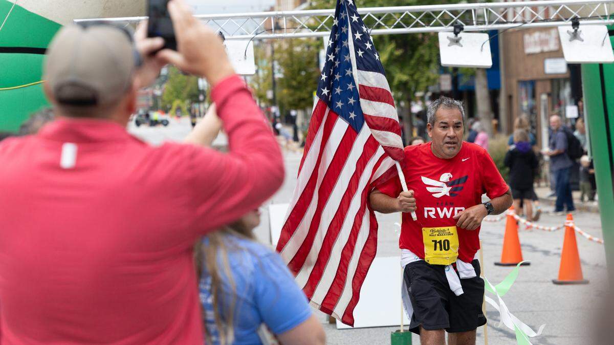 Joe Gomez, U.S. Navy veteran of Compton, Illinois, crosses the finish line at the Belleville Marathon on Sept. 28, 2024. Gomez carried the American flag as a representative for Team Red, White and Blue, a veterans group that emphasizes the benefits of physical exercise. “I did this for everyone who didn’t come home.”