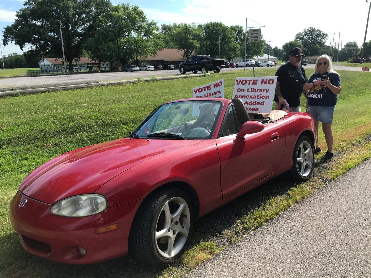 Jim Gunter and Toya Burdge discuss the proposed expansion of Millstadt Public Library on Tuesday in front of The Quail Club, where residents of Stookey 1 precinct vote. Burdge turned her car into a rolling billboard for the opposition.