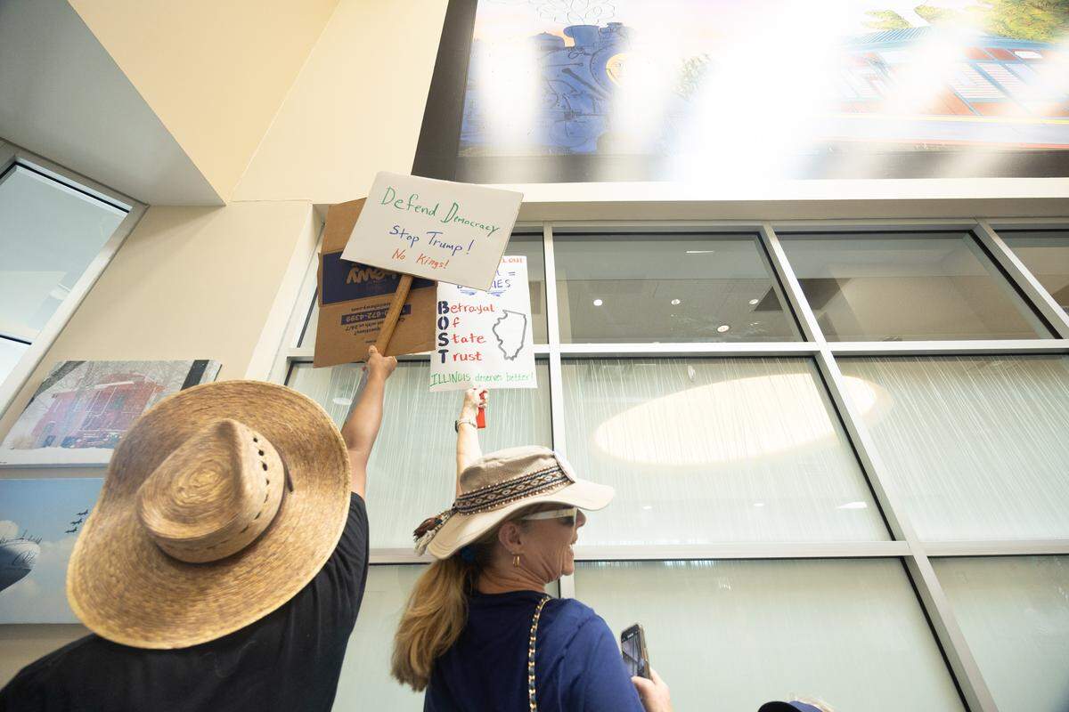 Protesters hold their signs up to the windows of the private meeting between U.S. Rep. Mike Bost and law enforcement at O’Fallon City Hall on Tuesday, Aug, 19.
