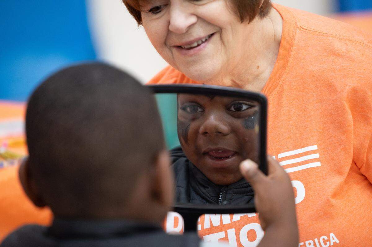 A child smiles into a mirror after having his face painted by Mary Bibi during a wear orange event hosted by Moms Demand Action.