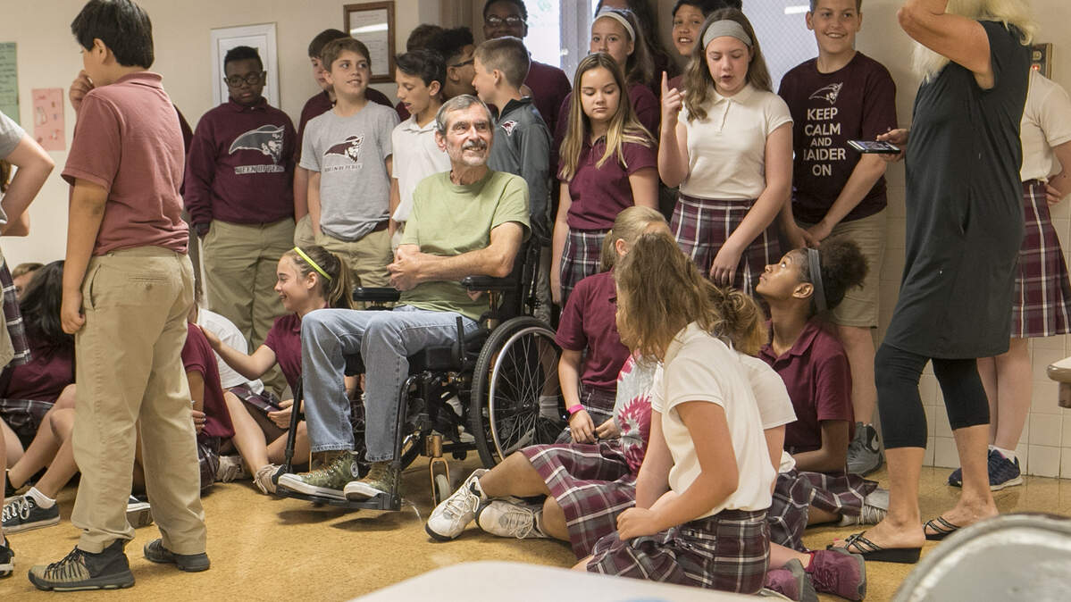 Art on the Square exhibitor Gary E. Bachers gets ready for a photo with sixth- and seventh-graders at Our Lady Queen of Peace School in Belleville on Friday after leading a presentation with his wife, Gabrielle. He creates intricate colored-pencil drawings, despite the fact that a massive stroke caused him to lose the ability to speak, write or use the right side of his body 31 years ago.
