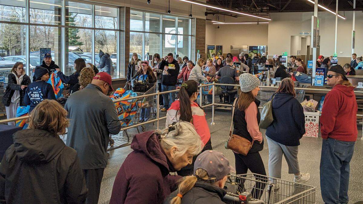 Customers continue entering the new Aldi store as others check out and collect tote bags on the way out.