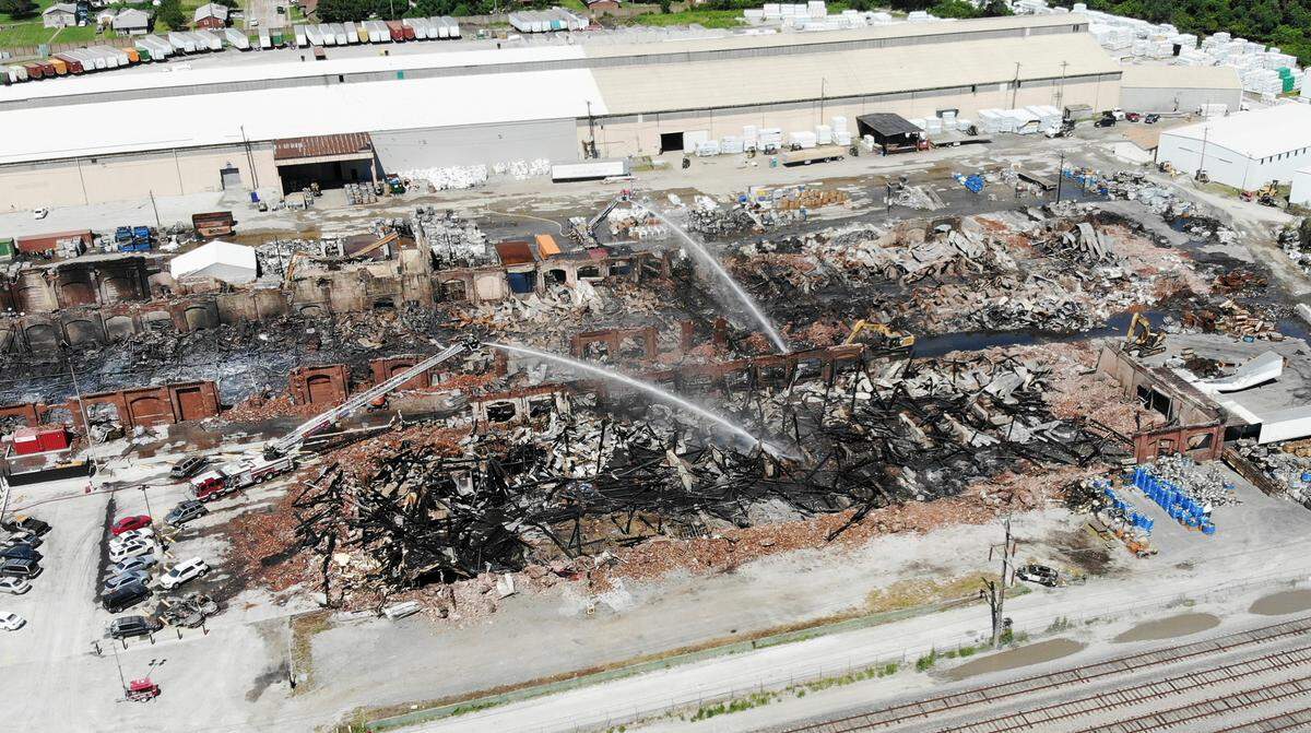 Two aerial fire trucks spray water on the remains of several building at Interco, a metaltronics recycling company in Madison, Illinois. At least two track hoes were working on the site. On Wednesday a fire destroyed several buildings on the campus.