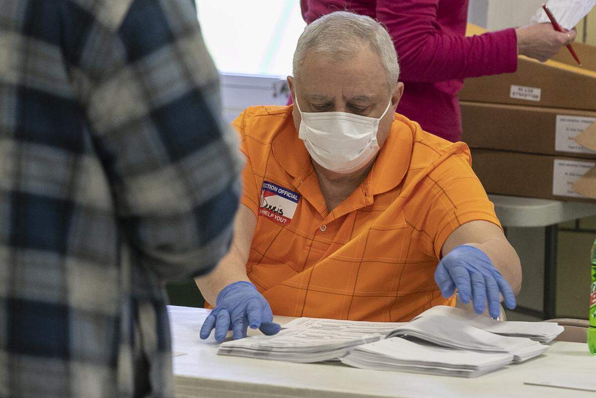 Election judge Dennis Geragosian looks for a voter’s registration card at the polling place inside Douglas Elementary School in Belleville during Tuesday’s primary election. Staff were using a variety of methods to disinfect and prevent the potential spread of coronavirus.