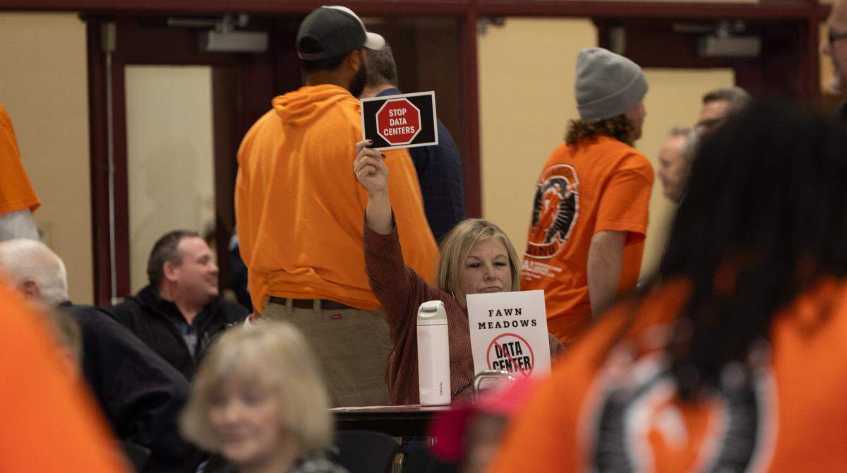 A resident of Fawn Meadows, a neighborhood adjacent to the possible data center location, holds up a sign reading “Stop data centers” while union members leave the meeting after hearing a steamfitters union representative advocate for the development.