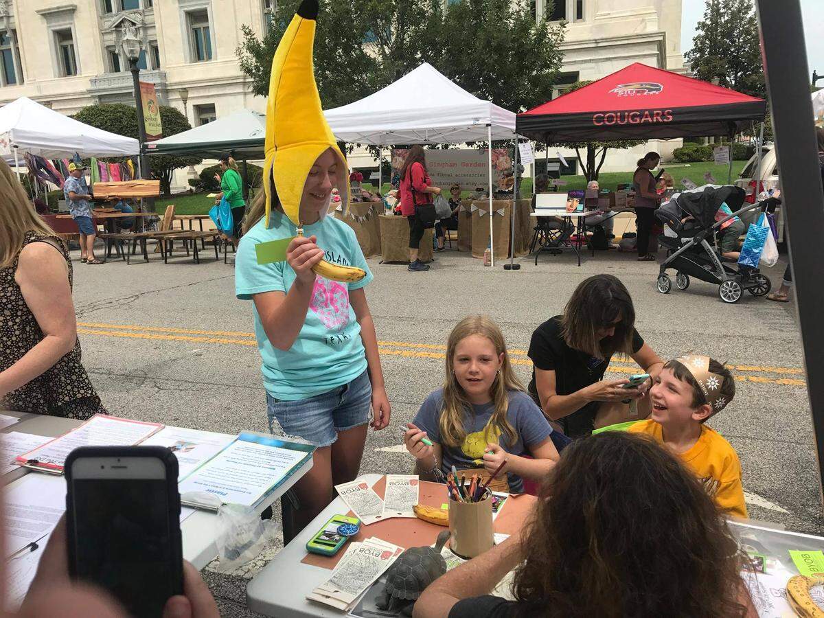 Kate Voss wears a banana head for a children’s activity at the Land of Goshen Community Market in Edwardsville. Her mother, Sheila, is a member of the Bring Your Own Glen-Ed group, which is trying to get people to shop with reusable bags.