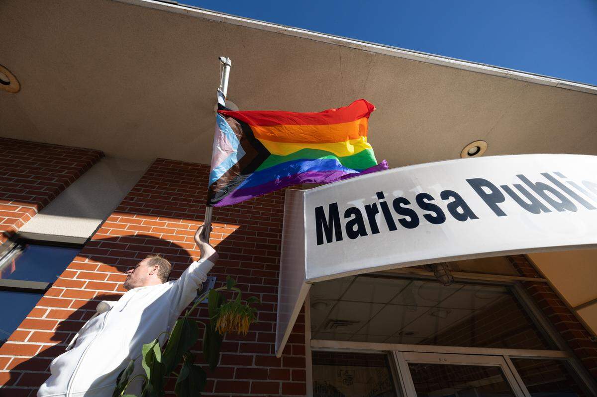 Riley Goodwin unfurls a pride flag that had gotten wound up on a windy afternoon at the Marissa, Ill. Public Library on Wednesday. An employee at the library said they put the flag up in support of Goodwin, who found a cross with an anti-gay slur on it on his property Tuesday. “I’ve never seen a pride flag in this town,” Goodwin said. “That means so much.”