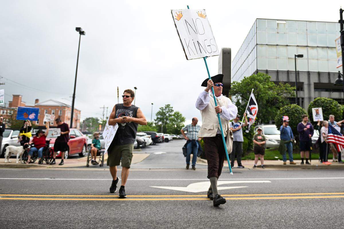 Patrick Hall, left, and Michael Bollmann, right, carry protest signs at the “No Kings” demonstration in Belleville’s Public Square Saturday, June 14, 2025.