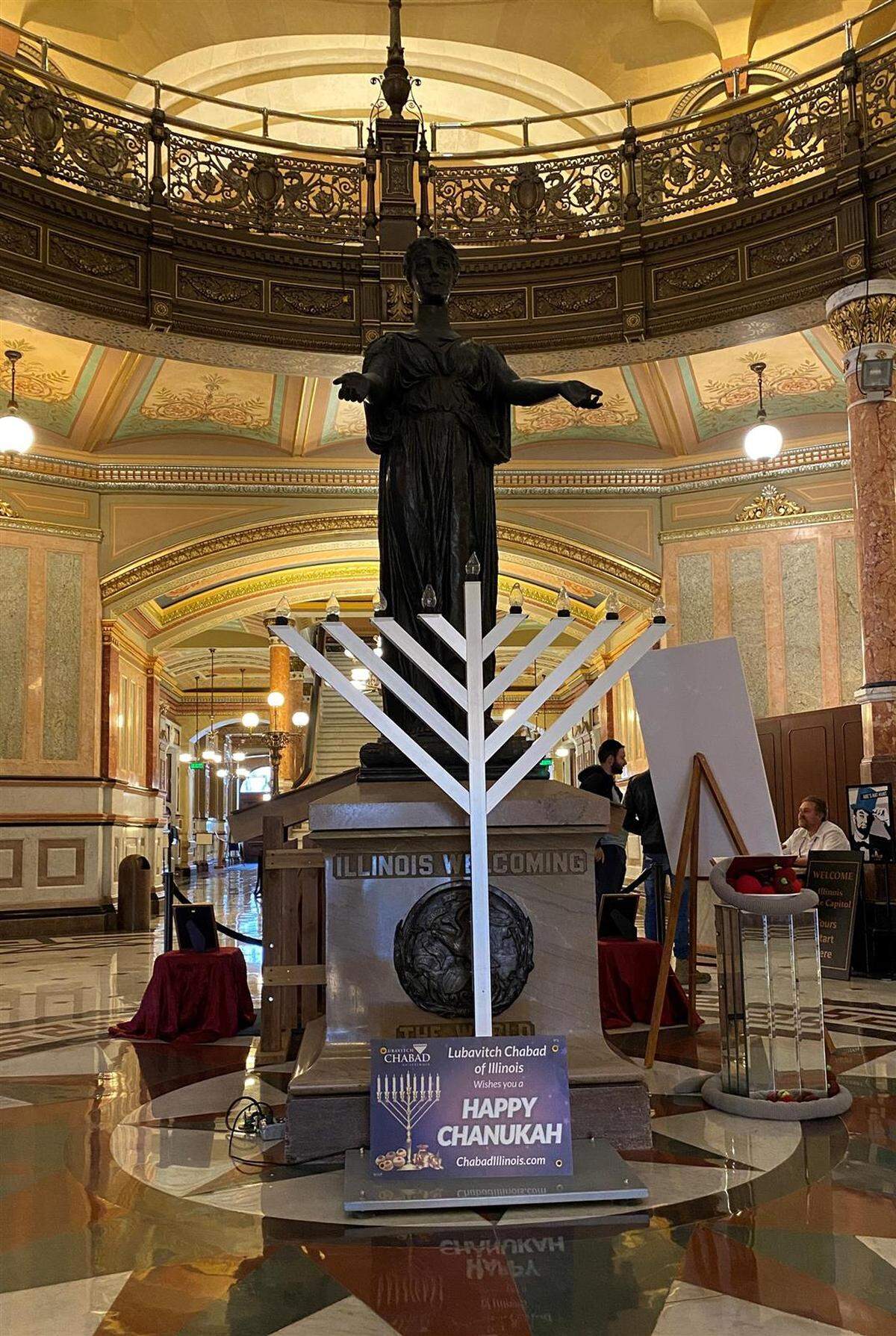 A member of the Satanic Temple of Illinois polishes the group’s 2022 holiday display on the Illinois Capitol rotunda. The display consists of a crocheted snake sitting on a book and a pile of apples crocheted by Temple members.