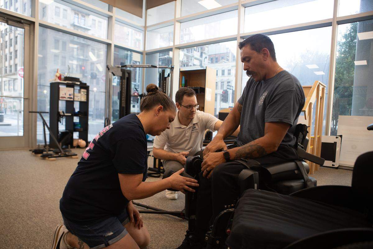 Brad Henke tightens a strap on his exoskeleton while his wife Patty and physical therapist Kevin Murray help during physical therapy in St. Louis. “It’s getting better every time,” Murray said when asked about Henke’s progress.