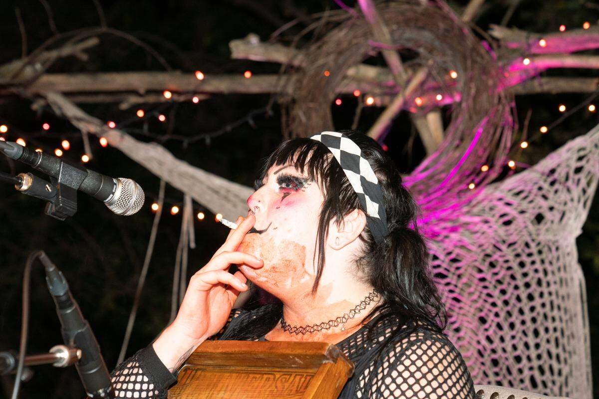 A washboard player in the folk-punk band Shrimps is Bugs smokes a cigarette in between sets at the Nunnery on Oct. 3, 2024. In the background, a crown of thorns mounted on the stage pays homage to the religious history of the location.
